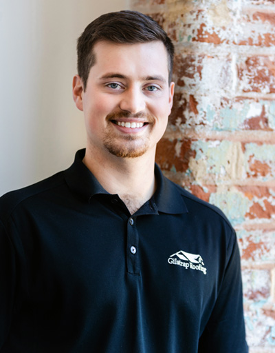Smiling man in navy Greenville roofing company polo shirt standing against exposed brick wall