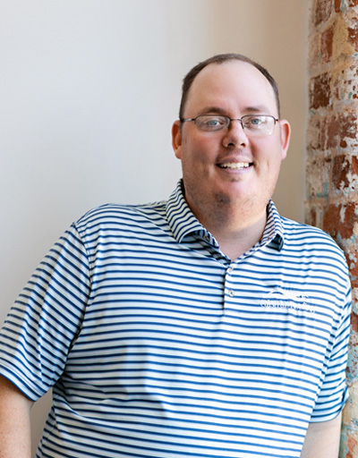 Smiling man wearing blue and white striped polo shirt and glasses, professional headshot for roofing and siding contractor in Greenville, South Carolina