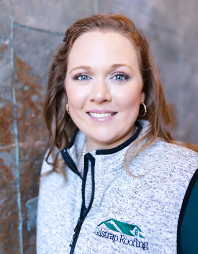 Woman smiling at camera wearing gray Austral Roofing vest over dark shirt, professional headshot for Greenville roofing contractor