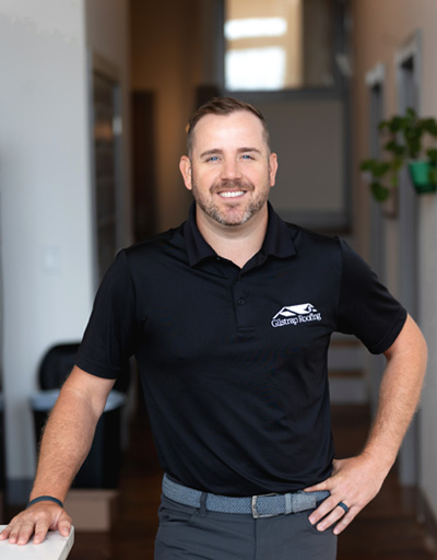 Professional roofing and siding contractor in Greenville, South Carolina, wearing black company polo shirt, smiling in office hallway