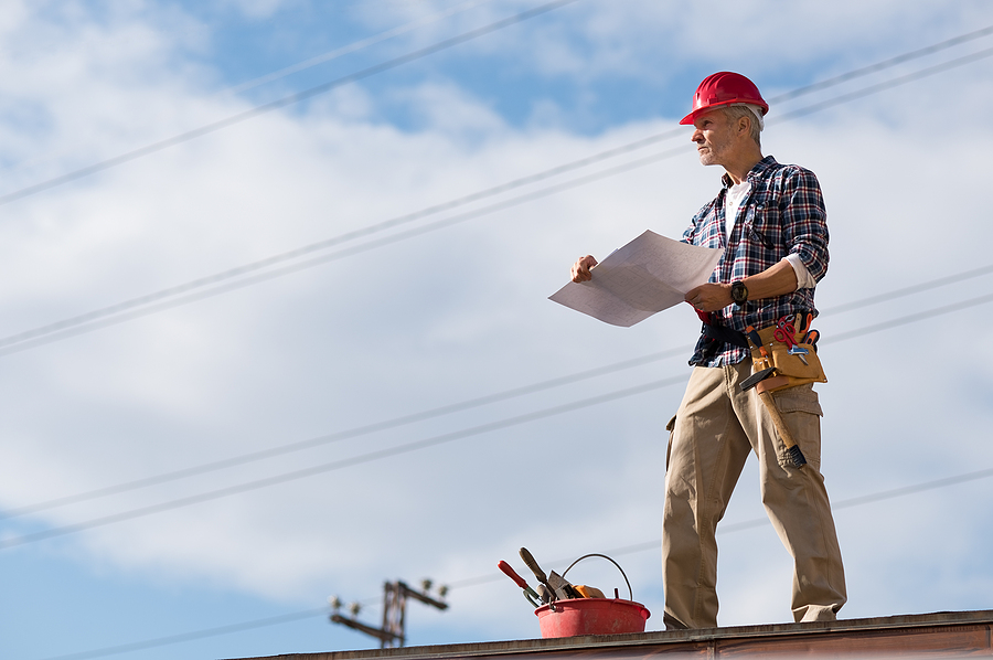 Engineer standing on rooftop looking away and holding blueprint project. Mature construction worker kit standing with copy space. Workman inspecting construction site with sheet of paper in hand.