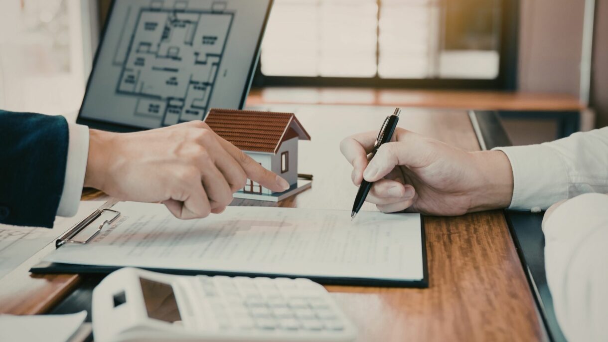 Real estate agent and customer reviewing roof replacement documents and house model at desk