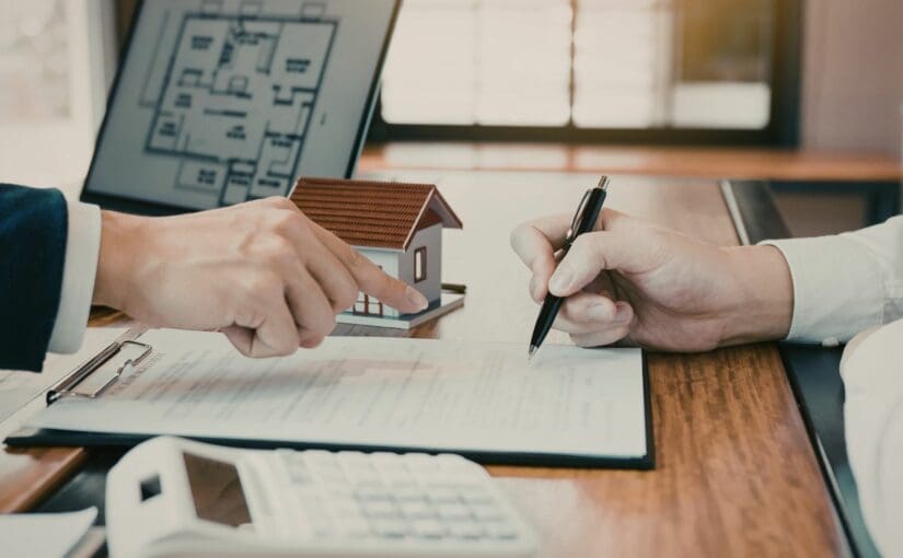Real estate agent and customer reviewing roof replacement documents and house model at desk