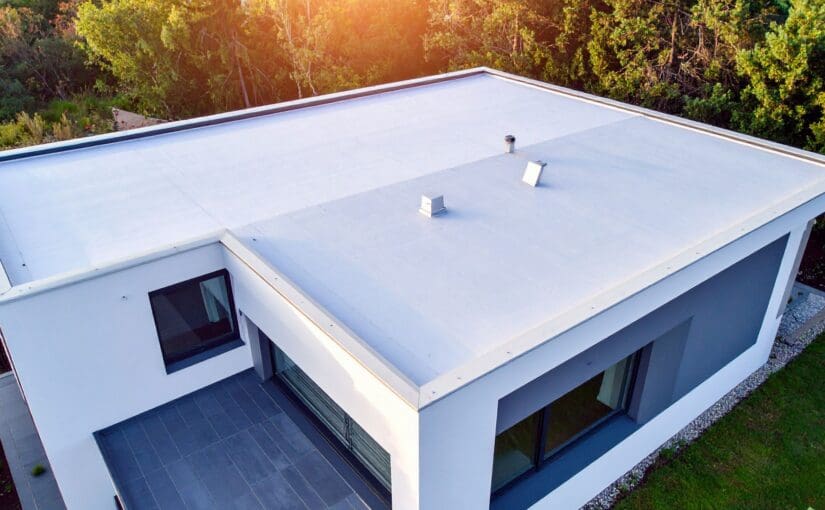 Modern residential home with flat white roof featuring ventilation boxes and skylights, surrounded by evergreen trees, showing contemporary roofing and construction design