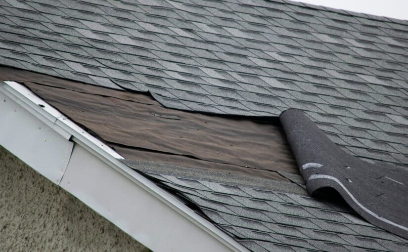 Damaged residential roof with exposed wood decking and missing shingles, showing storm damage requiring roof repair and inspection