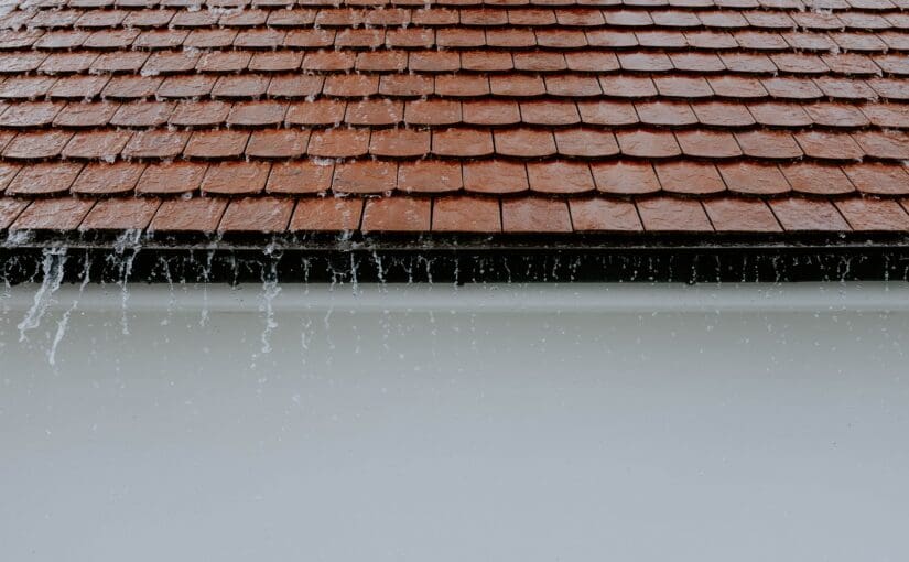Frozen icicles hanging from a dark gutter below damaged terra cotta roof shingles, indicating roof leak and winter weather damage requiring professional roof inspection and repair