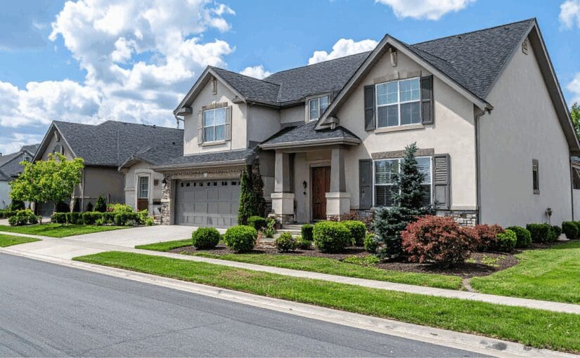 Two-story suburban home in Greenville, South Carolina with gray shingle roof, cream siding, stone accents, and manicured landscaping featuring shrubs and trees